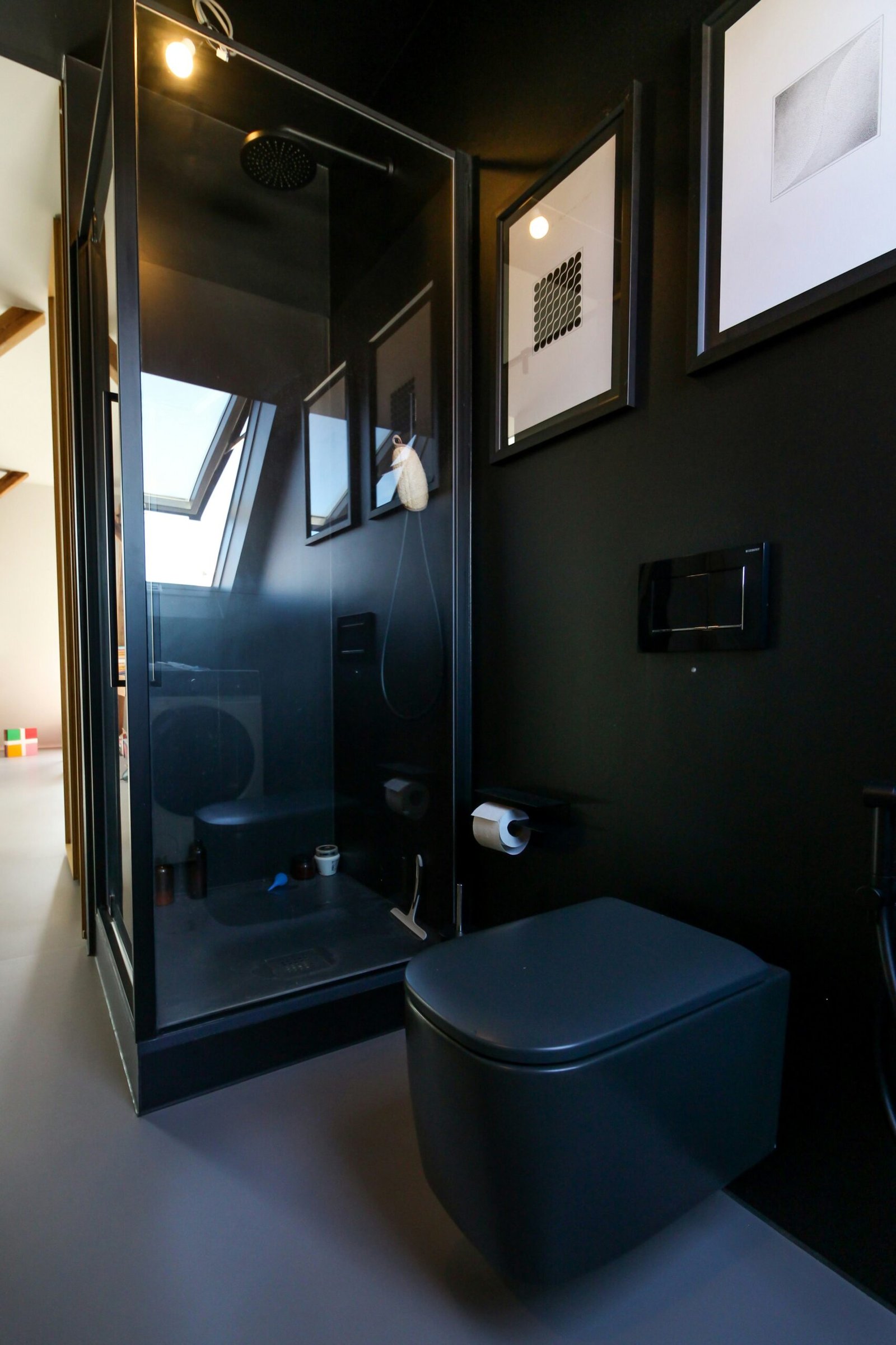 une salle de bains noir et grise composé d'un wc suspendu noir et d'un receveur de douche noir avec mitigeur noir
