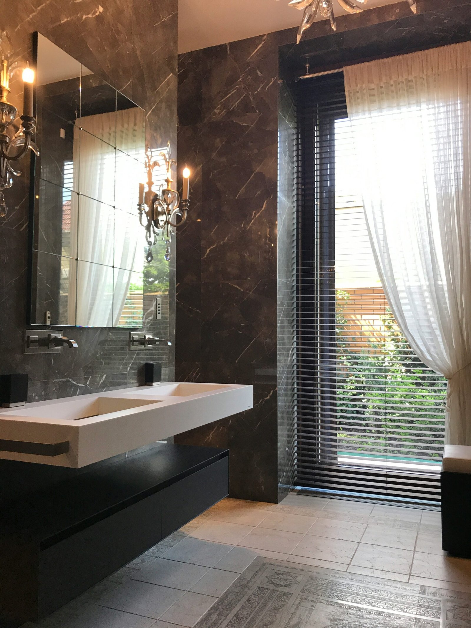 une salle de bains design avec mur en marbre et double vasque en pierre avec robienterie et tuyauterie intégrès donnant l'acces aisé a une personne à mobilité réduite