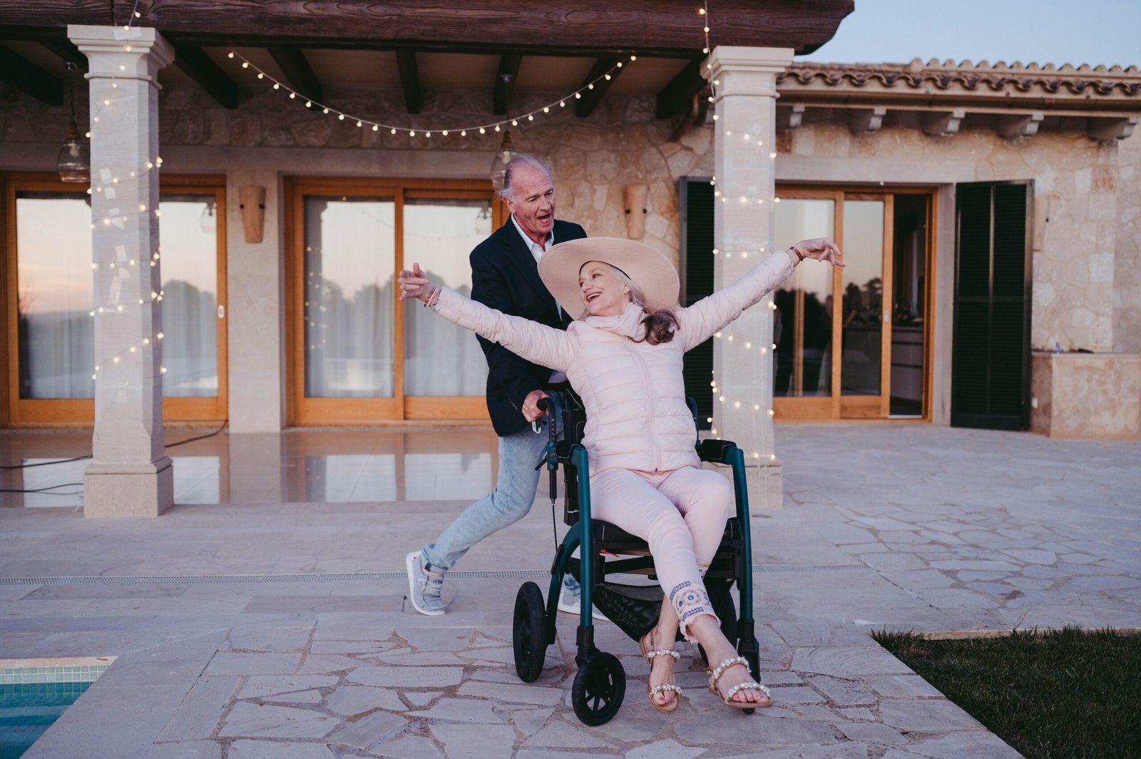 une dame heureuse en fauteuil roulant qui rigole avec son mari qui la pousse sur la terrasse de leur maison