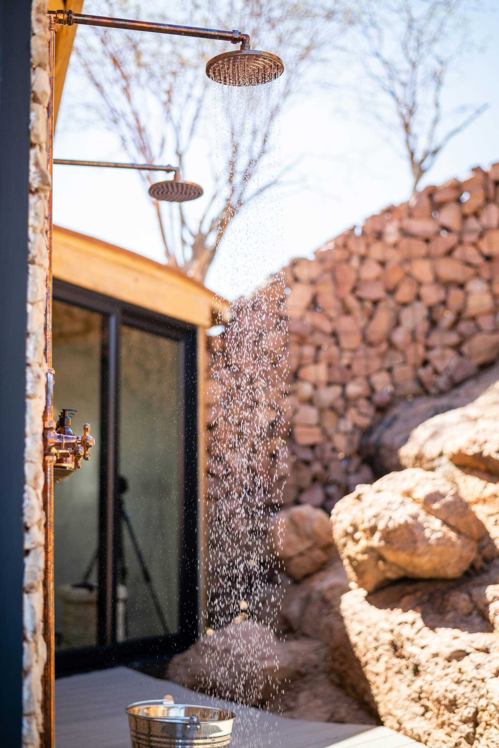 Une belle réalisation d'une double douche tout en cuivre à extérieur sur une terrasse niché au coeur des rochers avec de l'eau qui coule depuis l'un des pommeaux